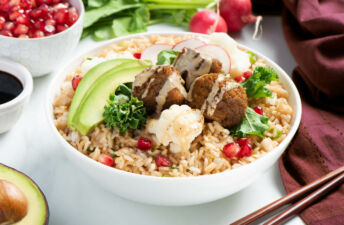 White bowl filled with fried rice, kale, deep fried falafel, avocado and pomegranate seeds topped with tahini sauce